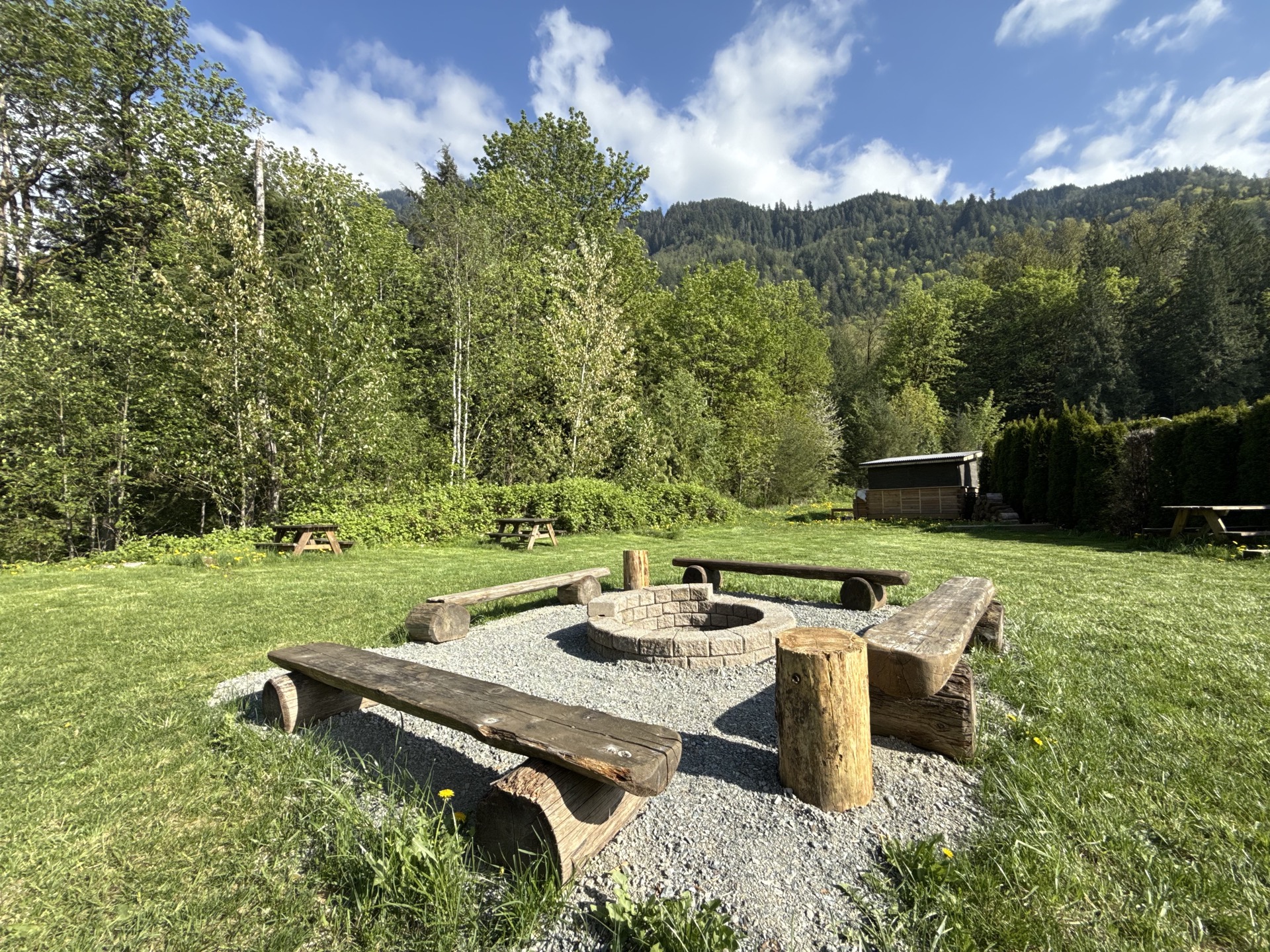 A log-bench fire pit circle on the lawn, ringed by forest and mountains