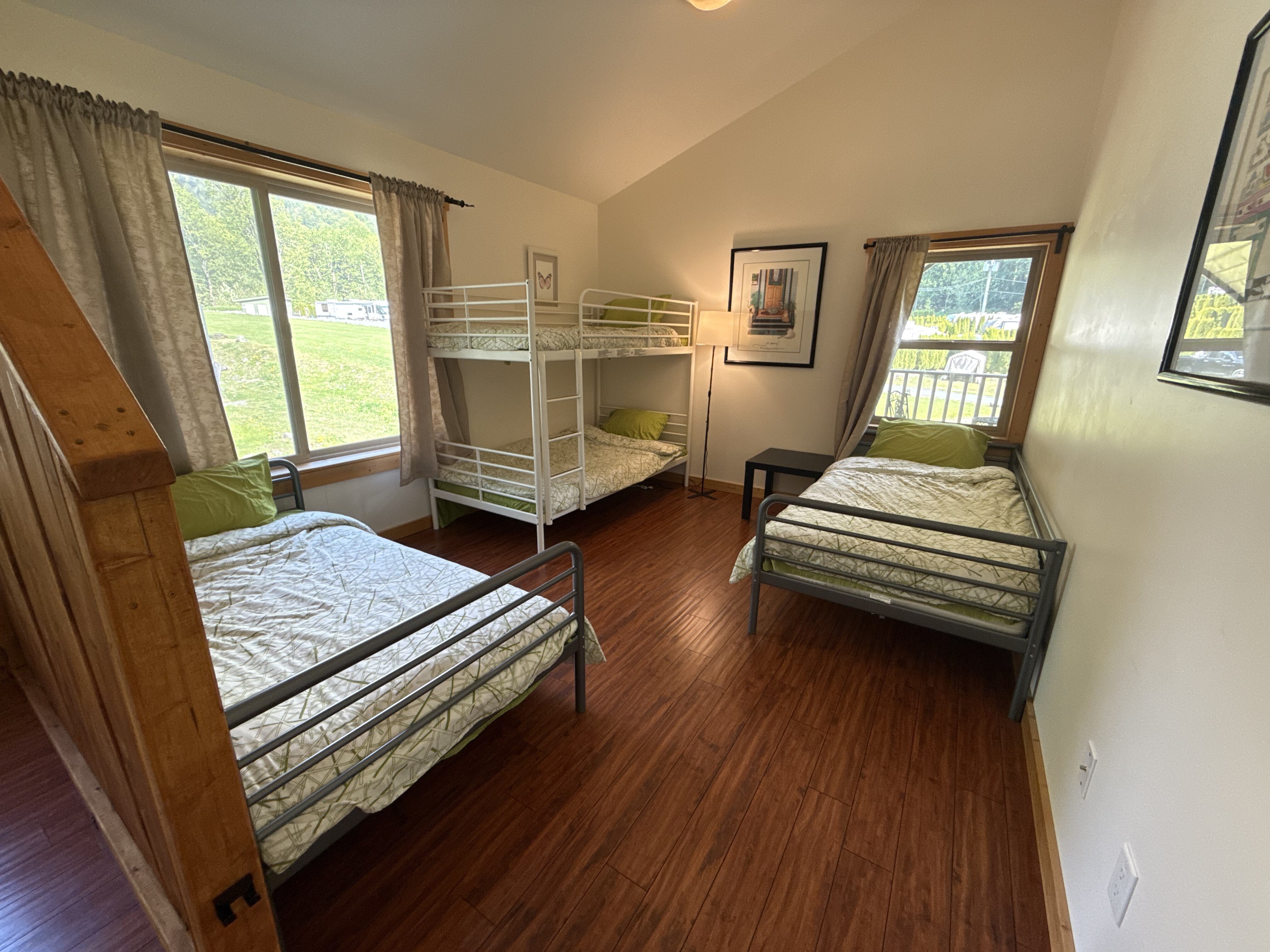 Bright lodge bedroom with bunks and twin beds, windows onto the lawn