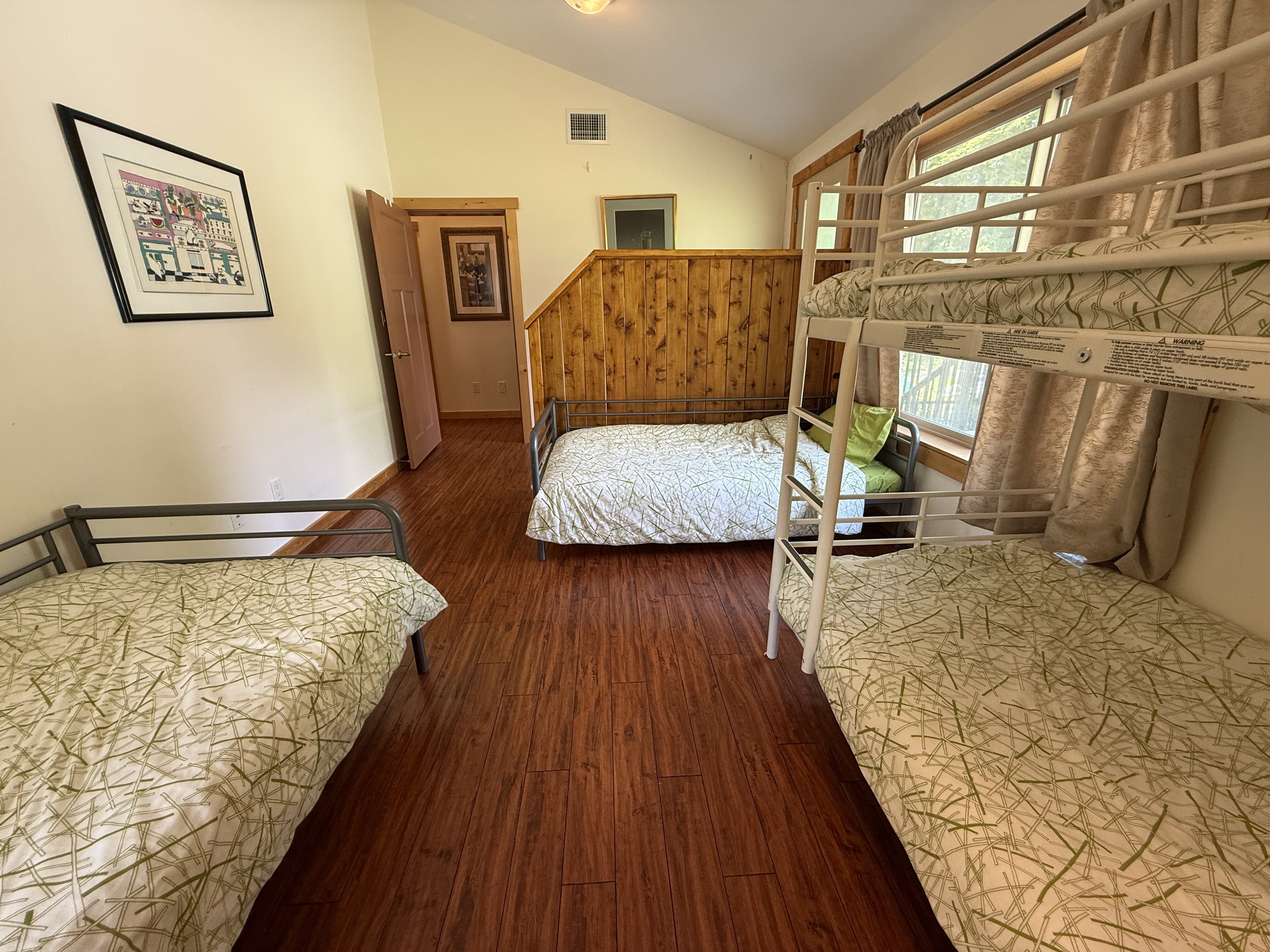 A bright suite bedroom with bunks and twin beds, windows onto the lawn